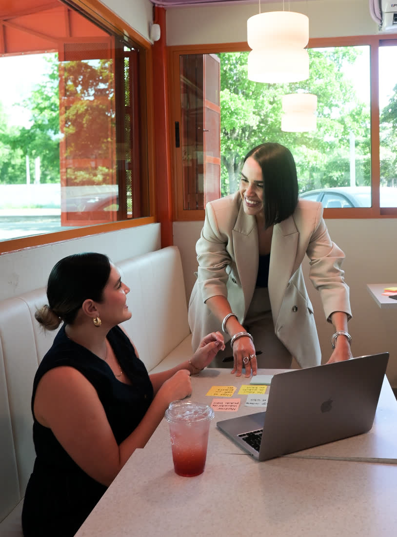 Dos mujeres conversan en una mesa de restaurante con una laptop